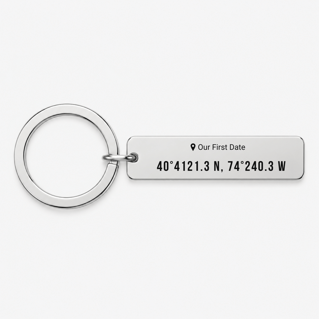 A silver metal keychain featuring a rectangular tag engraved with the text 'Our First Date' and coordinates '40° 4121.3 N, 74° 240.