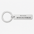 A silver metal keychain featuring a rectangular tag engraved with the text 'Our First Date' and coordinates '40° 4121.3 N, 74° 240.
