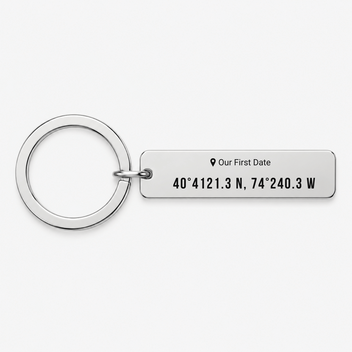 A silver metal keychain featuring a rectangular tag engraved with the text 'Our First Date' and coordinates '40° 4121.3 N, 74° 240.