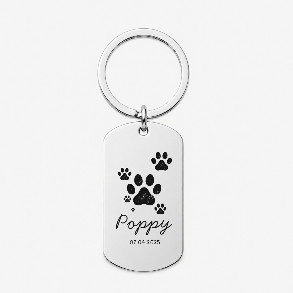 A personalized silver dog tag keychain with a circular split ring, featuring black paw prints, the name 'Poppy' in cursive, and the date '07.04.