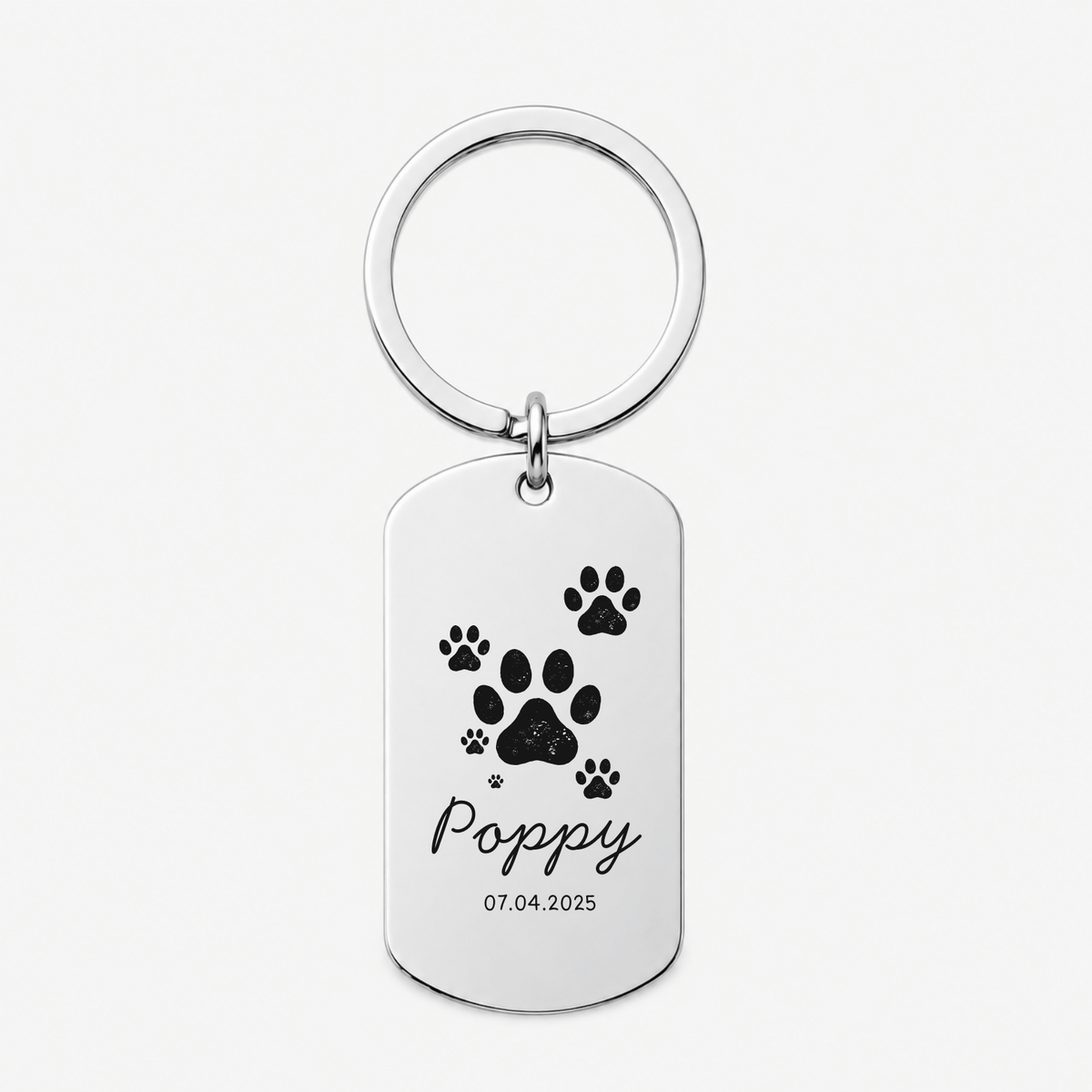 A personalized silver dog tag keychain with a circular split ring, featuring black paw prints, the name 'Poppy' in cursive, and the date '07.04.