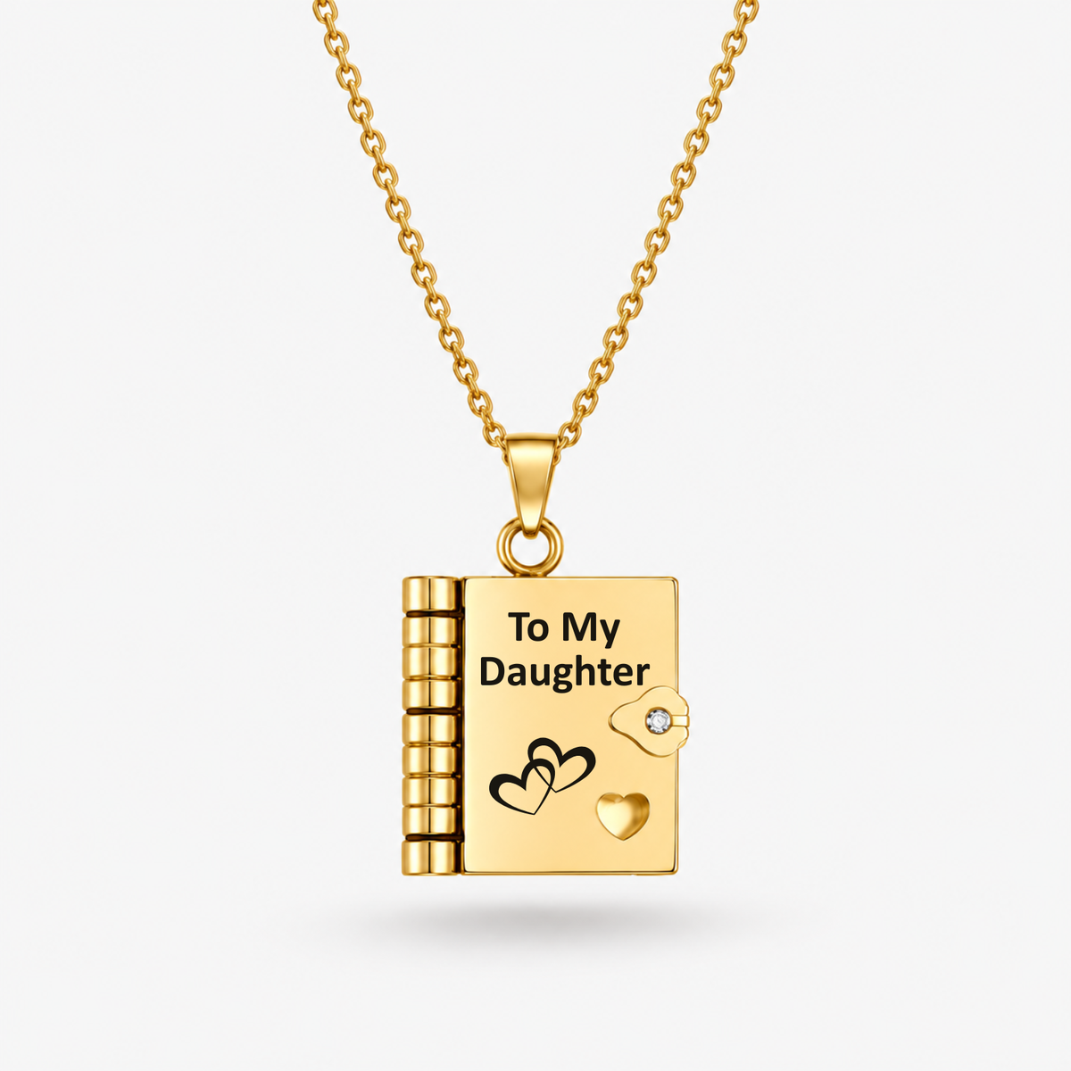 A gold keepsake book pendant necklace engraved with 'To My Daughter' and heart designs, suspended from a gold chain against a light gray background.