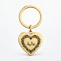 A gold heart-shaped keychain with a black floral border and Arabic script on a clean white background.