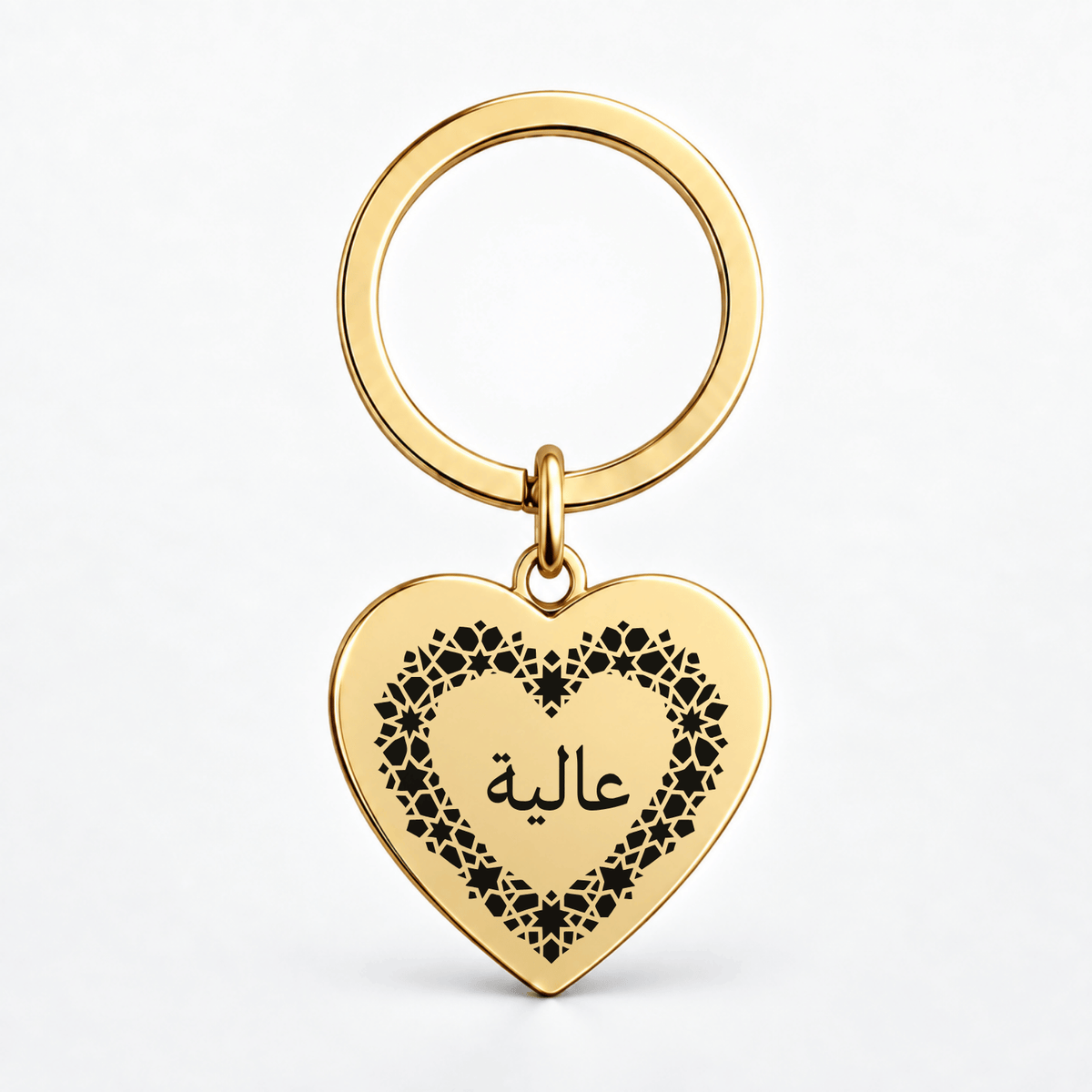 A gold heart-shaped keychain with a black floral border and Arabic script on a clean white background.