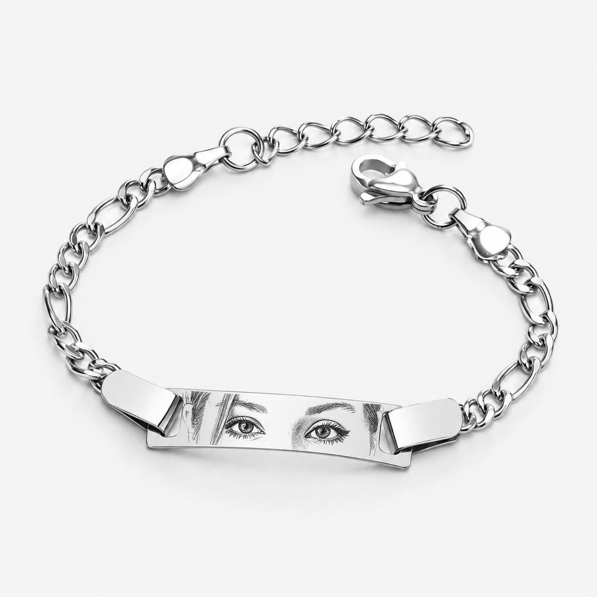 A silver-toned metal bracelet featuring a central rectangular bar engraved with a stylized pair of eyes, connected to a curb chain with a heart-shaped extender and clasp, shown on a light gray background.