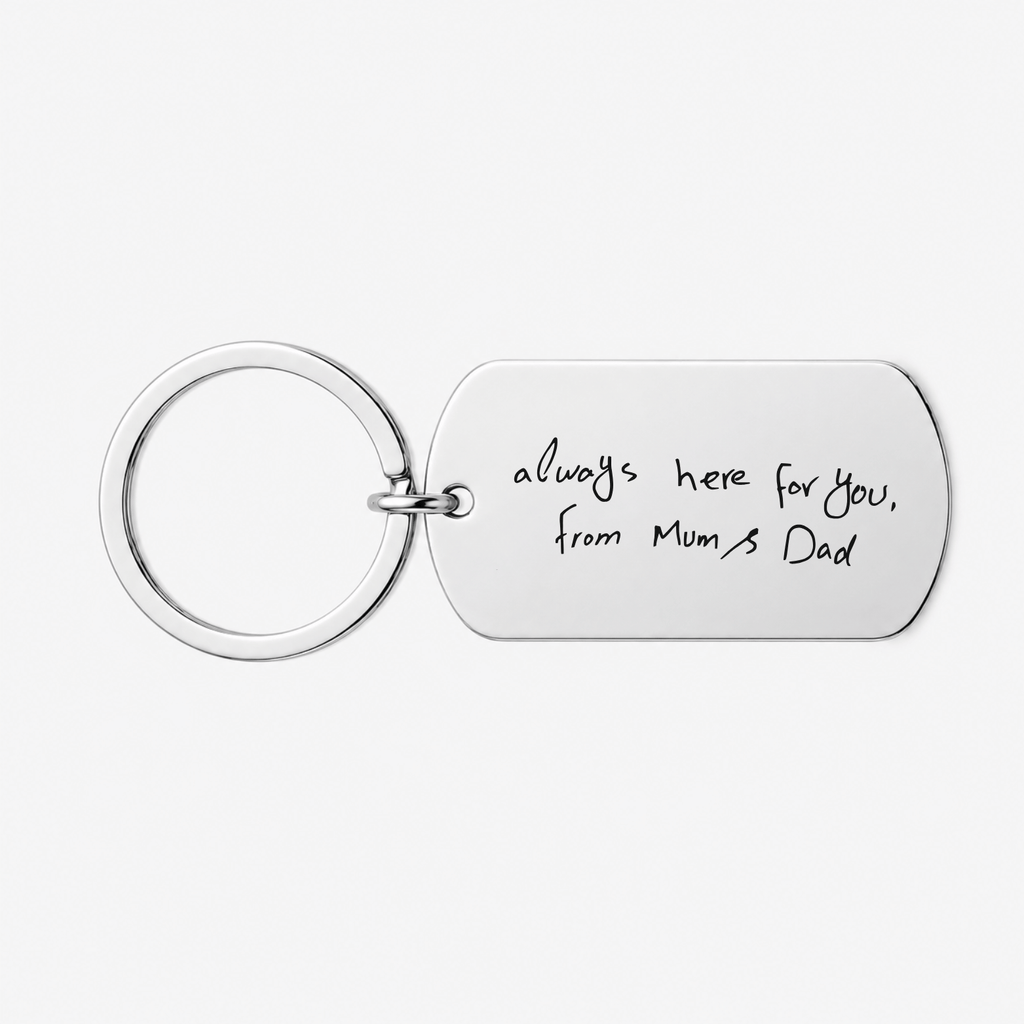 A silver metal keychain with a rectangular tag engraved with the handwritten text 'always here for you, from Mum's Dad' on a light gray background.