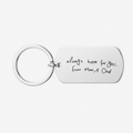 A silver metal keychain with a rectangular tag engraved with the handwritten text 'always here for you, from Mum's Dad' on a light gray background.